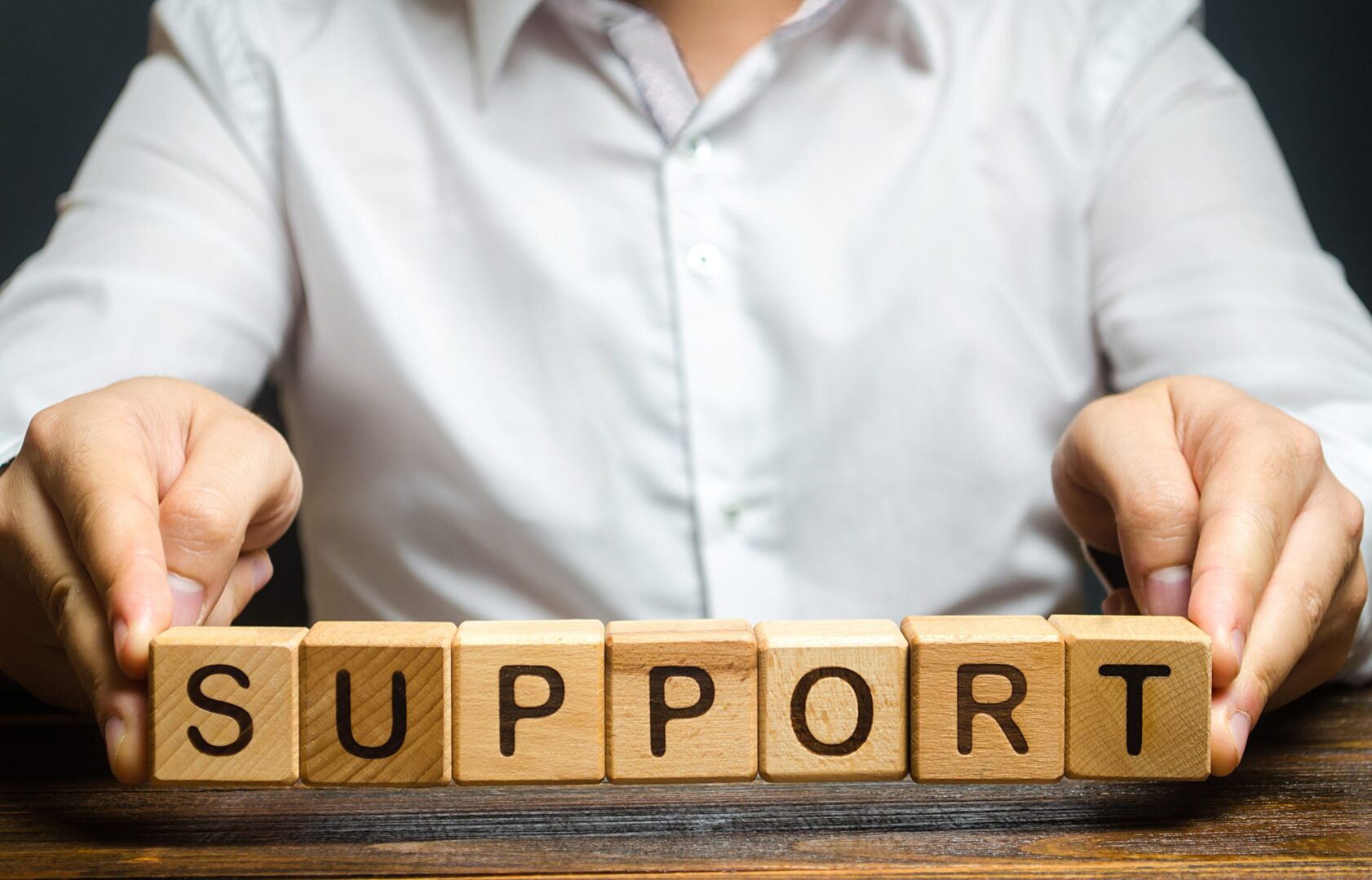 A man's hands arranging wooden blocks to spell out the word SUPPORT