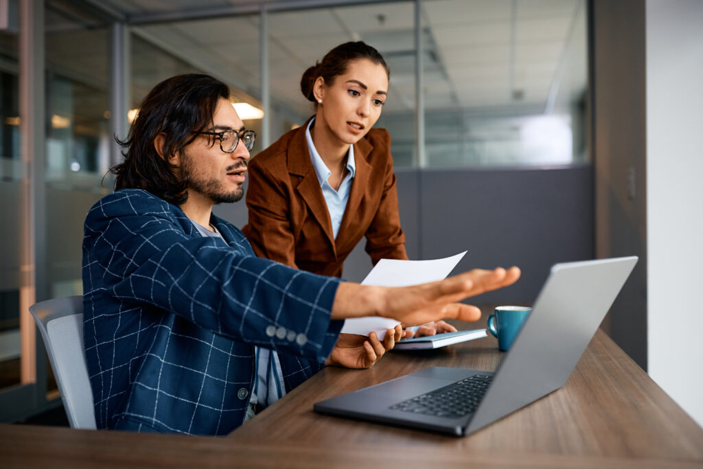 Young businessman and his female colleague talking while working on a computer in the office.